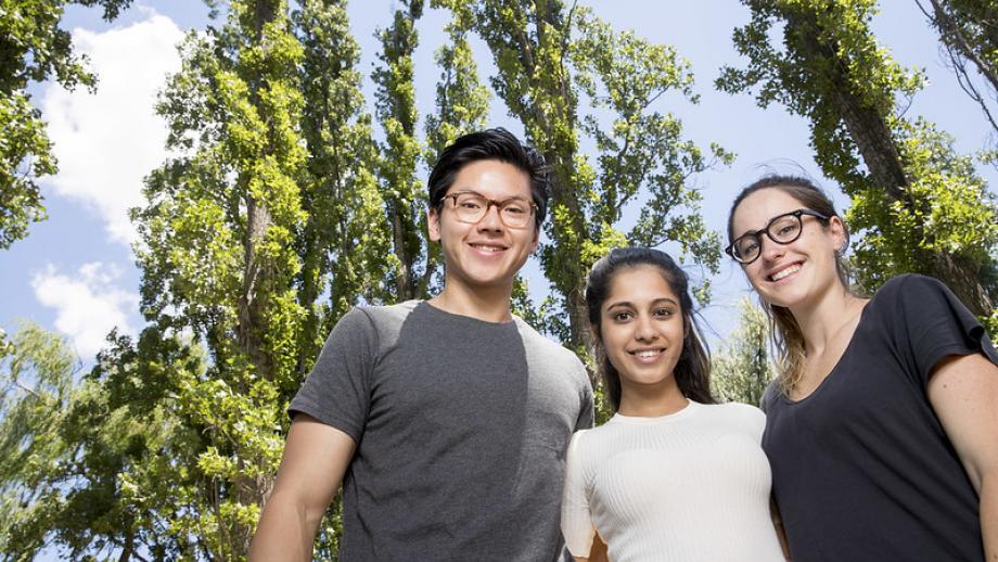 Three students looking down at the camera with trees and blue sky in the background